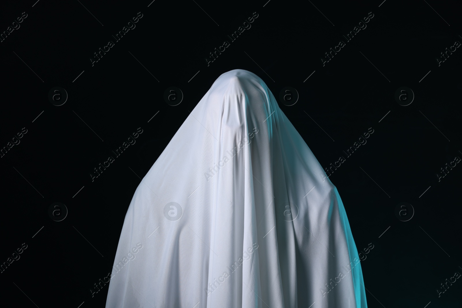 Photo of Creepy ghost. Man covered with white sheet on black background