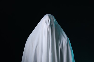 Photo of Creepy ghost. Man covered with white sheet on black background