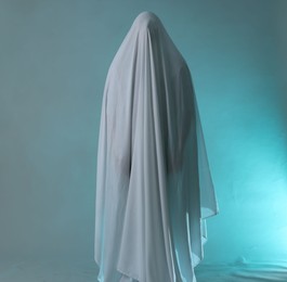 Photo of Creepy ghost. Man covered with white sheet in smoke on light blue background