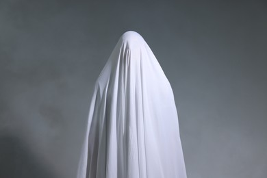 Photo of Creepy ghost. Man covered with white sheet in smoke on light grey background