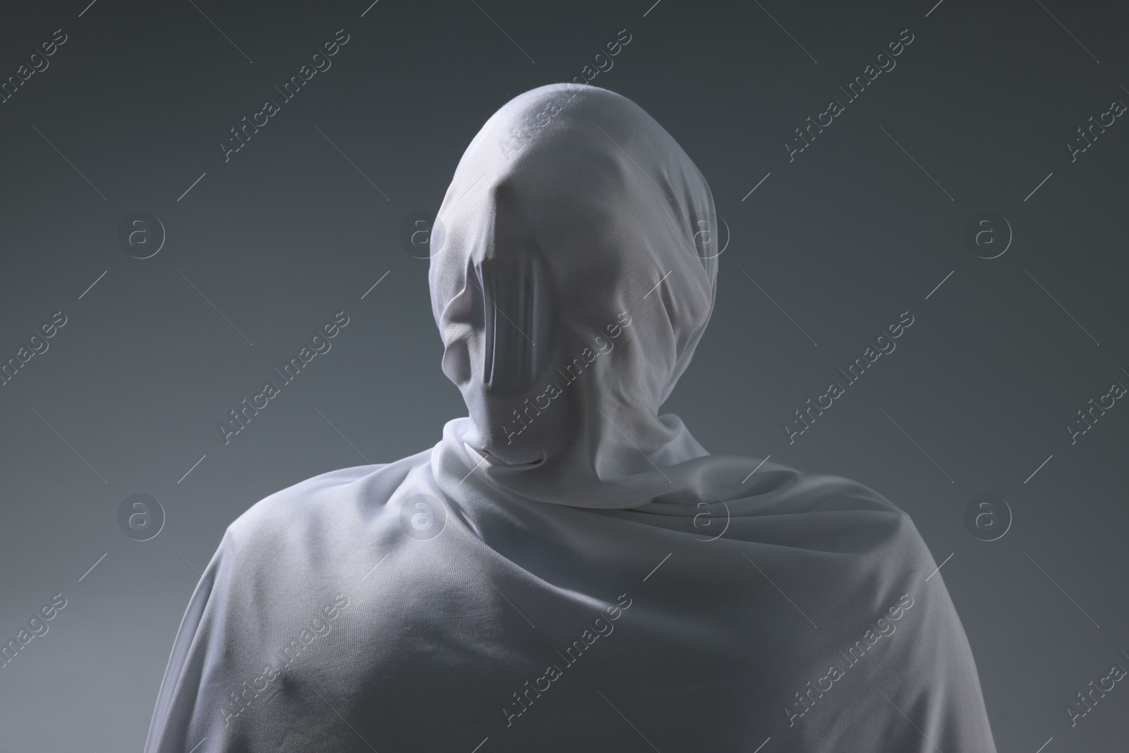 Creepy ghost. Man covered with white sheet on light grey background Photo of Creepy ghost. Man covered with white sheet on light grey background