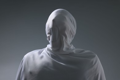 Photo of Creepy ghost. Man covered with white sheet on light grey background