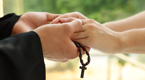 Photo of Priest and woman holding hands outdoors, closeup
