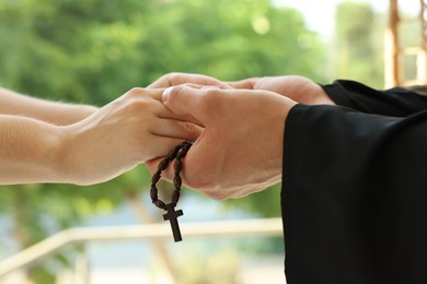 Photo of Priest and woman holding hands outdoors, closeup