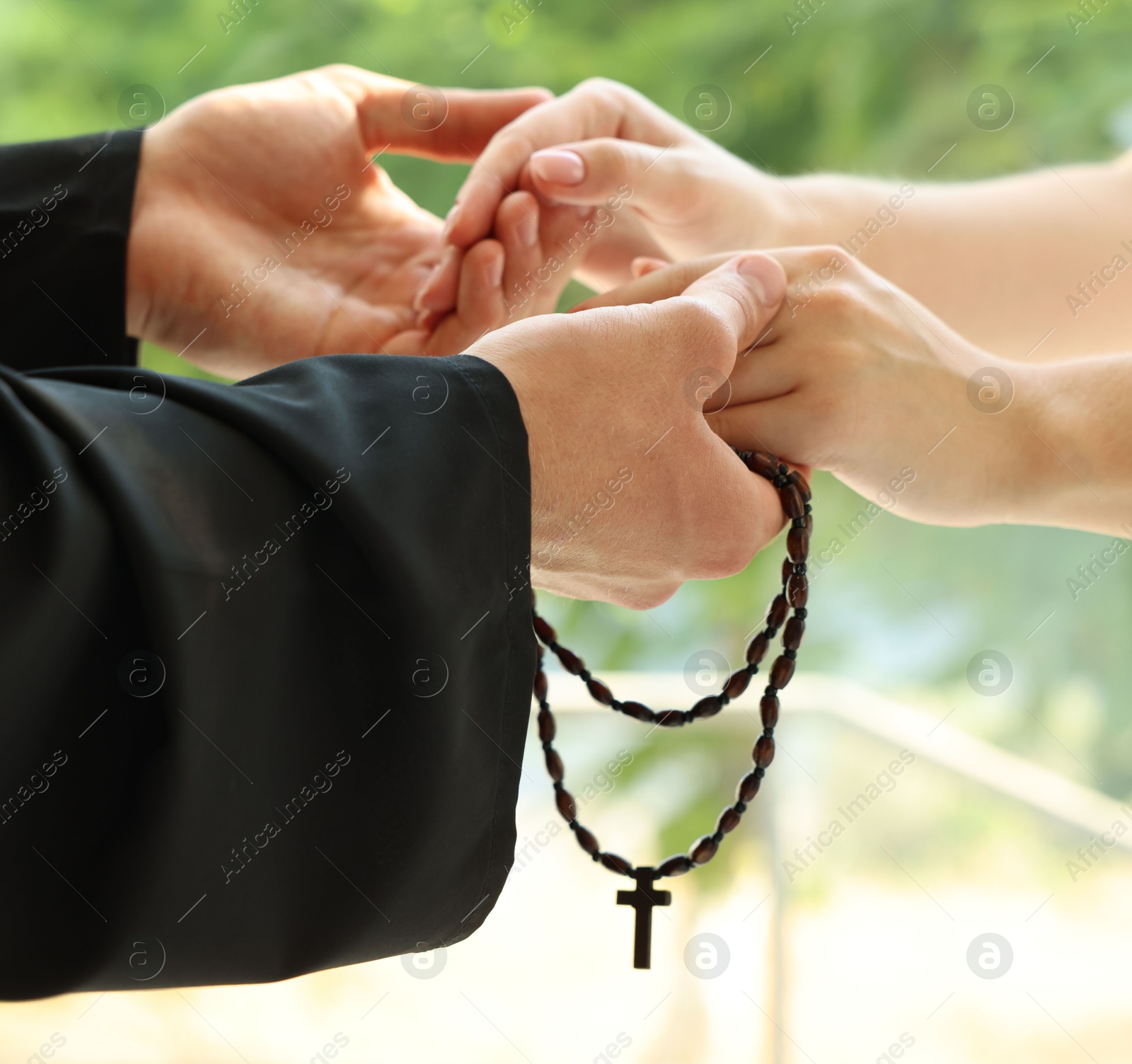 Photo of Priest and woman holding hands outdoors, closeup