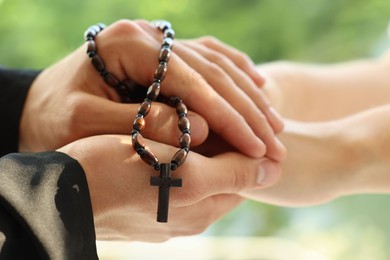 Photo of Priest and woman holding hands outdoors, closeup
