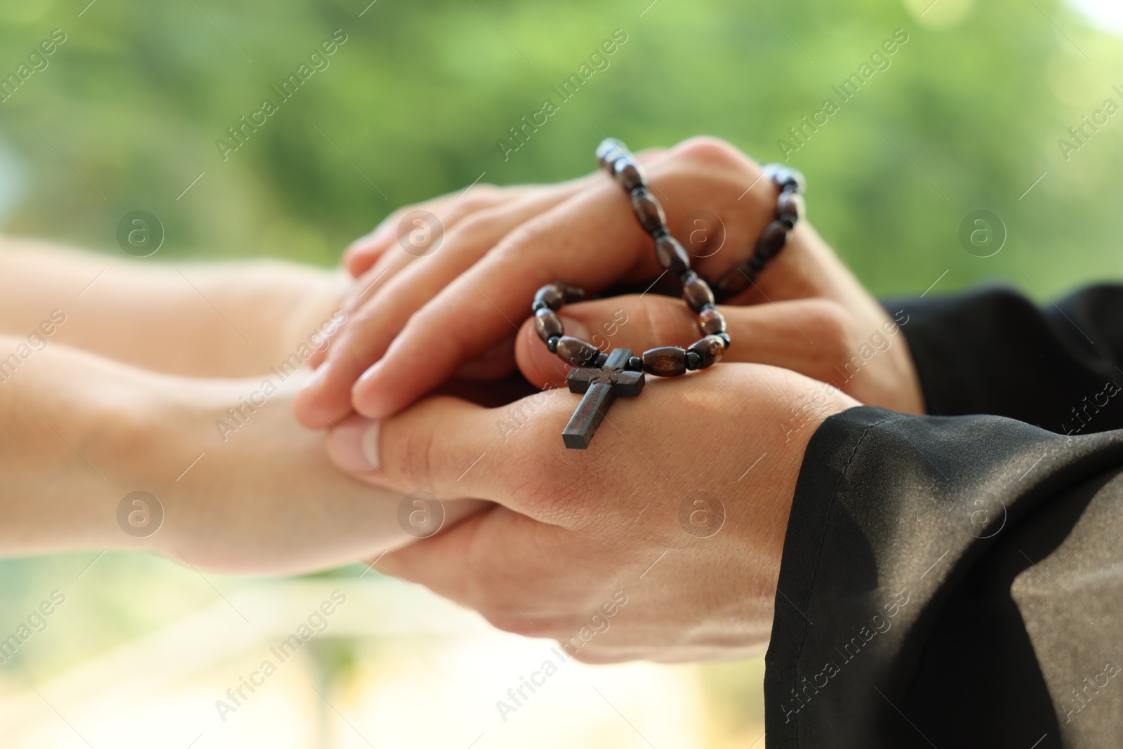 Photo of Priest and woman holding hands outdoors, closeup