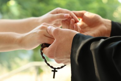 Photo of Priest and woman holding hands outdoors, closeup