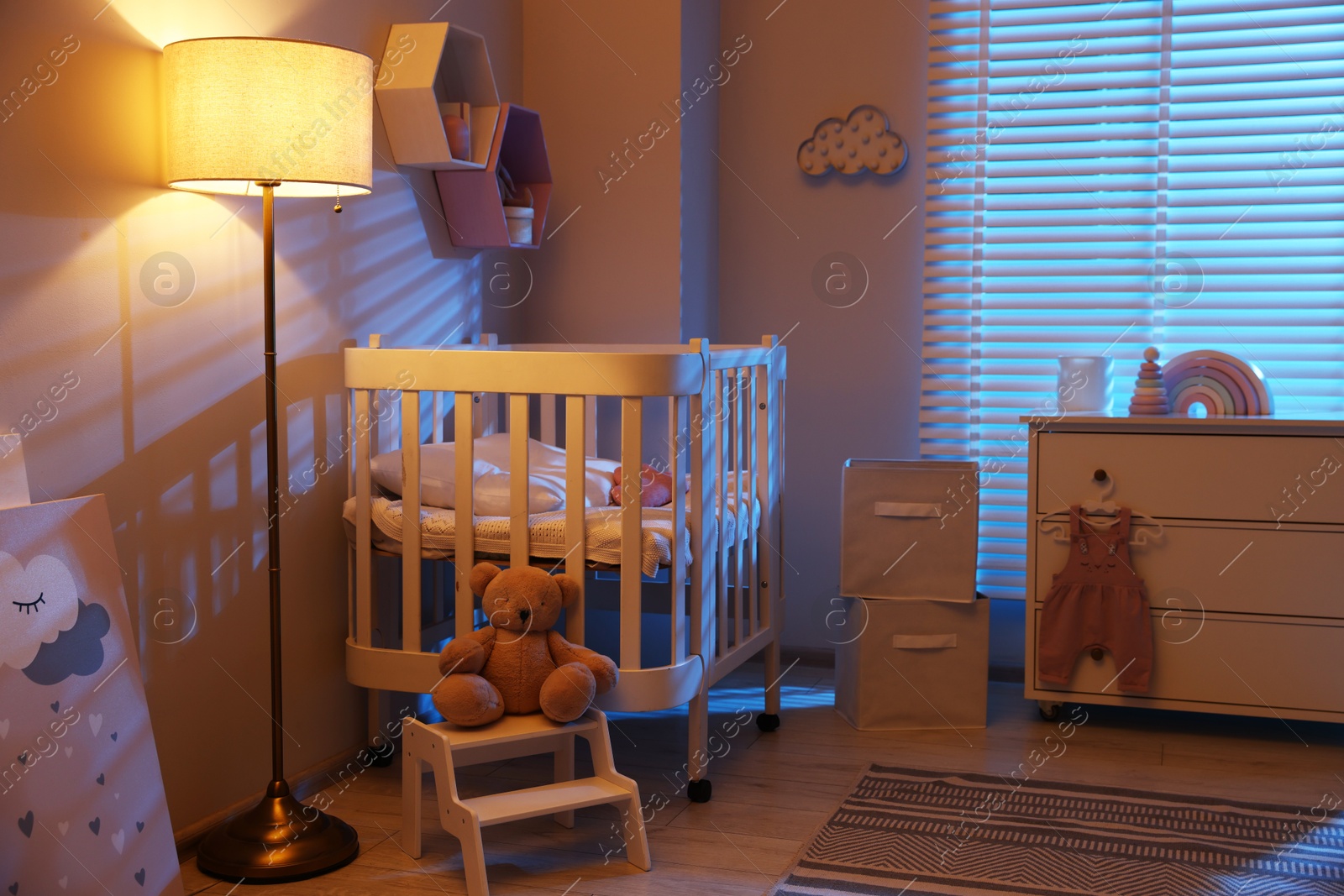 Stylish baby room with comfortable crib and other furniture in evening. Interior design Photo of Stylish baby room with comfortable crib and other furniture in evening. Interior design