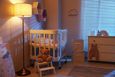Photo of Stylish baby room with comfortable crib and other furniture in evening. Interior design