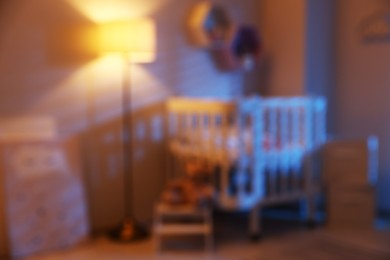 Photo of Baby room with comfortable crib and other furniture in evening, blurred view. Interior design