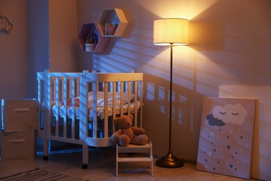 Photo of Stylish baby room with comfortable crib and other furniture in evening. Interior design