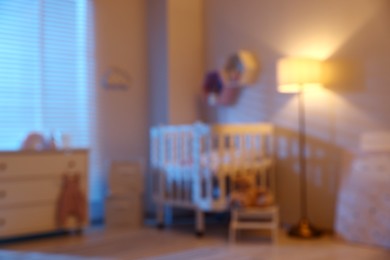 Photo of Baby room with comfortable crib and other furniture in evening, blurred view. Interior design