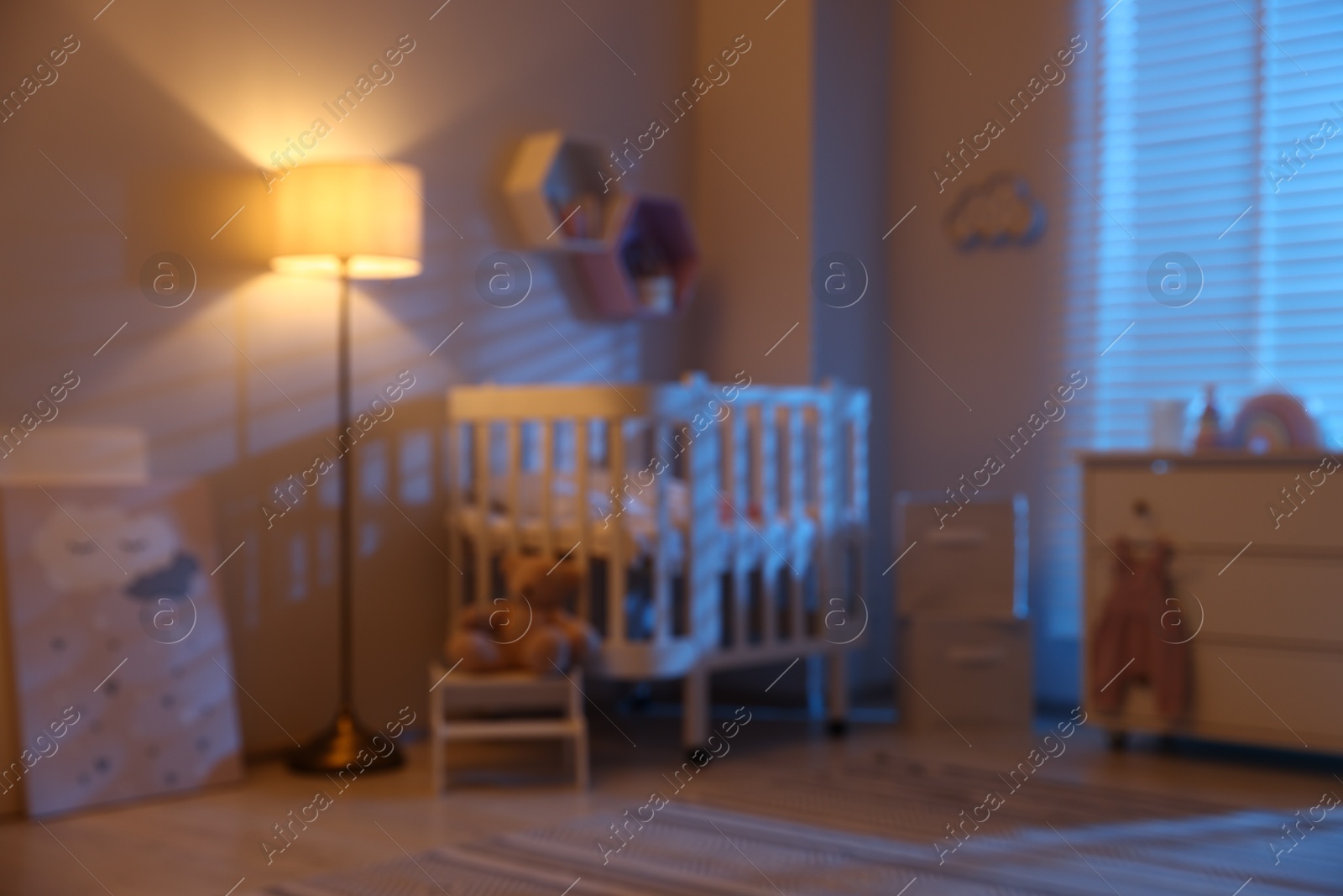 Stylish baby room with comfortable crib and other furniture in evening, blurred view. Interior design Photo of Stylish baby room with comfortable crib and other furniture in evening, blurred view. Interior design