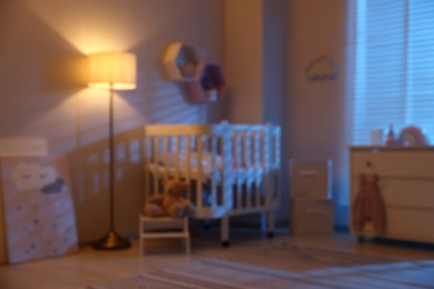 Photo of Stylish baby room with comfortable crib and other furniture in evening, blurred view. Interior design