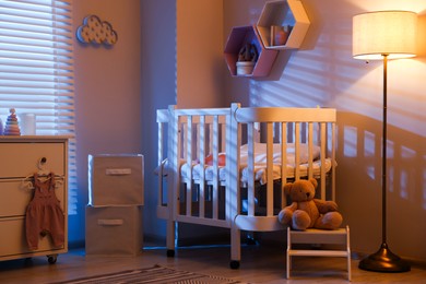 Photo of Stylish baby room with comfortable crib and other furniture in evening. Interior design