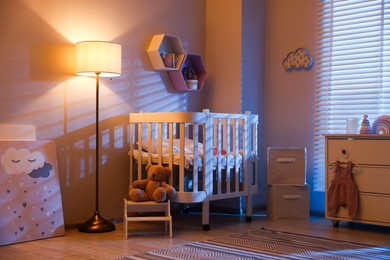 Photo of Stylish baby room with comfortable crib and other furniture in evening. Interior design