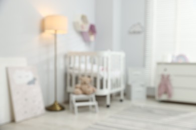 Photo of Baby room with comfortable crib and other furniture, blurred view. Interior design