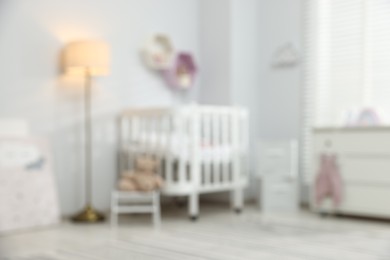 Photo of Cozy baby room with crib and decor elements, blurred view. Interior design