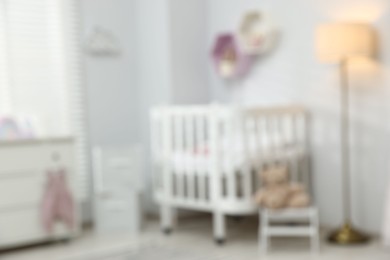 Photo of Cozy baby room with crib and decor elements, blurred view. Interior design