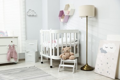 Photo of Stylish white crib, chest of drawers, lamp, toys and decor elements in baby's room. Interior design