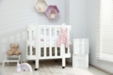 Photo of Baby room interior with comfortable crib and other furniture, blurred view