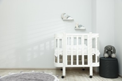 Photo of Stylish baby room interior with comfortable crib, pouf and toys. Space for text