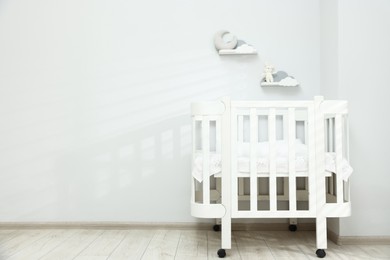 Photo of Comfortable crib near white wall in baby's room, space for text. Interior design