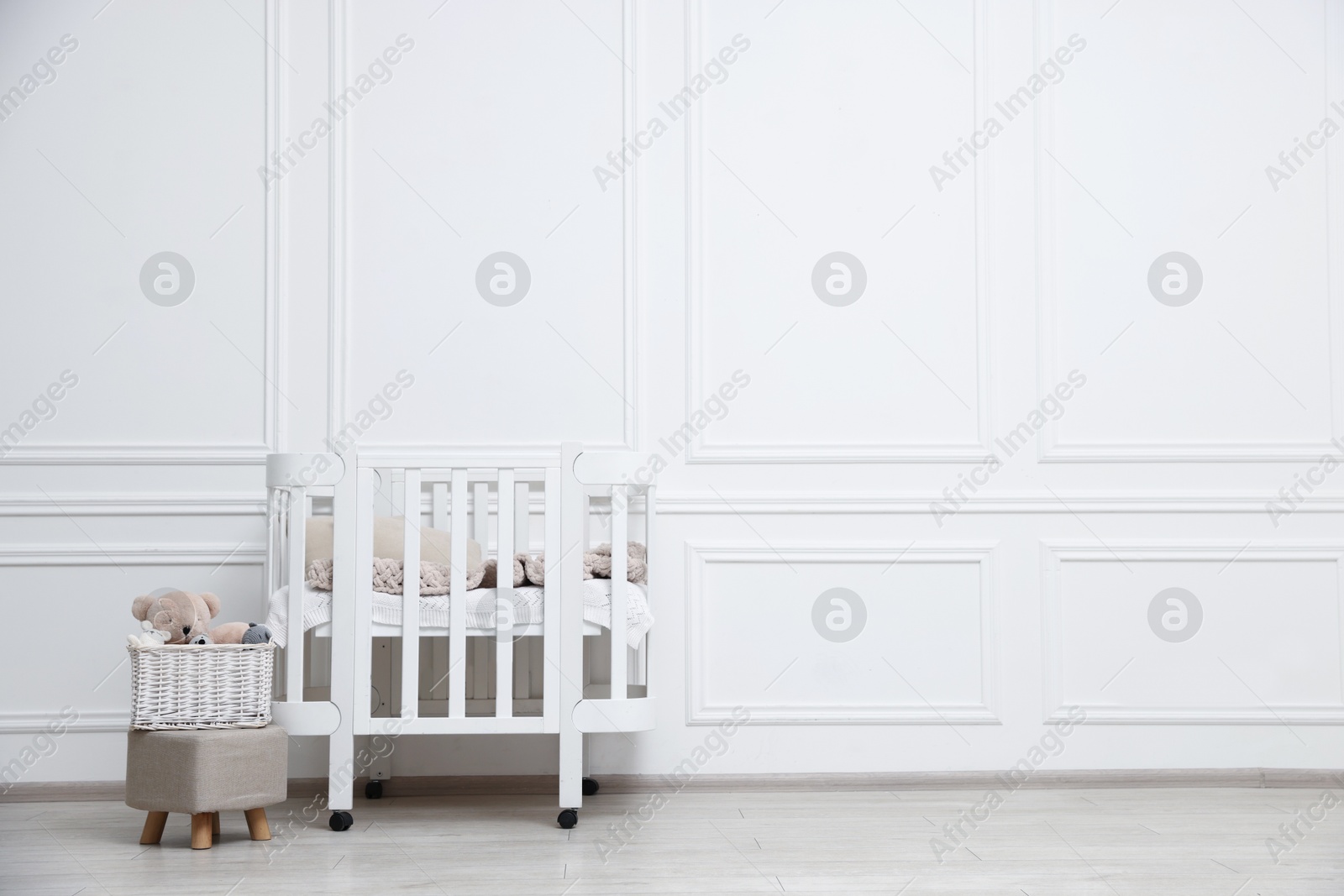 Comfortable crib, pouf and toys near white wall in baby's room, space for text. Interior design Photo of Comfortable crib, pouf and toys near white wall in baby's room, space for text. Interior design