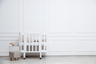 Photo of Comfortable crib, pouf and toys near white wall in baby's room, space for text. Interior design