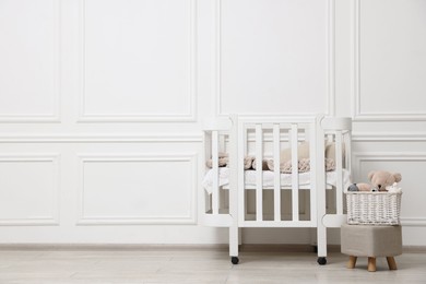 Photo of Comfortable crib, pouf and toys near white wall in baby's room, space for text. Interior design