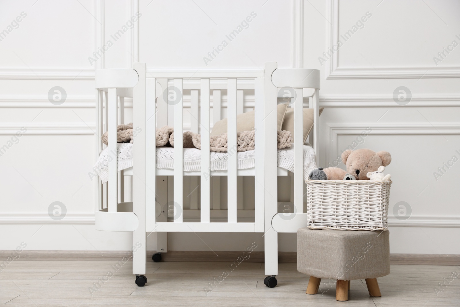 Comfortable crib, pouf and toys near white wall in baby's room. Interior design Photo of Comfortable crib, pouf and toys near white wall in baby's room. Interior design