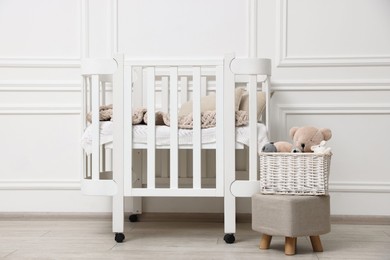 Photo of Comfortable crib, pouf and toys near white wall in baby's room. Interior design