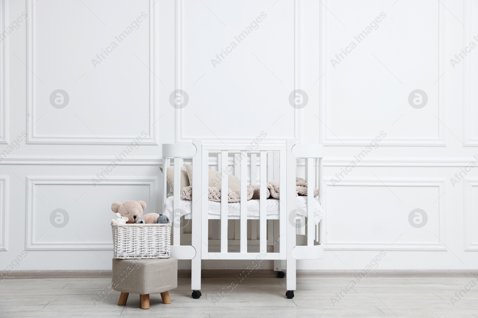 Comfortable crib, pouf and toys near white wall in baby's room. Interior design Photo of Comfortable crib, pouf and toys near white wall in baby's room. Interior design