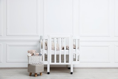 Photo of Comfortable crib, pouf and toys near white wall in baby's room. Interior design