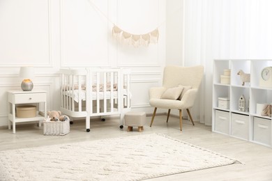 Photo of Stylish baby room interior with comfortable crib, armchair and toys