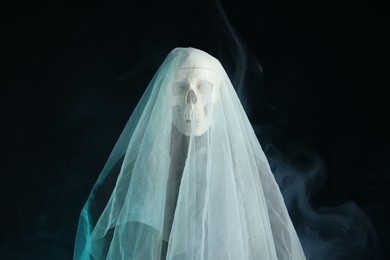 Photo of Creepy ghost. Skeleton covered with white sheet in smoke on black background