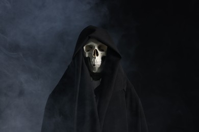 Photo of Creepy ghost. Skeleton covered with sheet in smoke on black background
