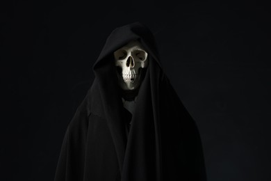 Photo of Creepy ghost. Skeleton covered with sheet on black background