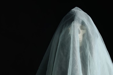 Photo of Creepy ghost. Skeleton covered with white sheet on black background, space for text