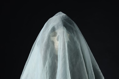 Photo of Creepy ghost. Skeleton covered with white sheet on black background