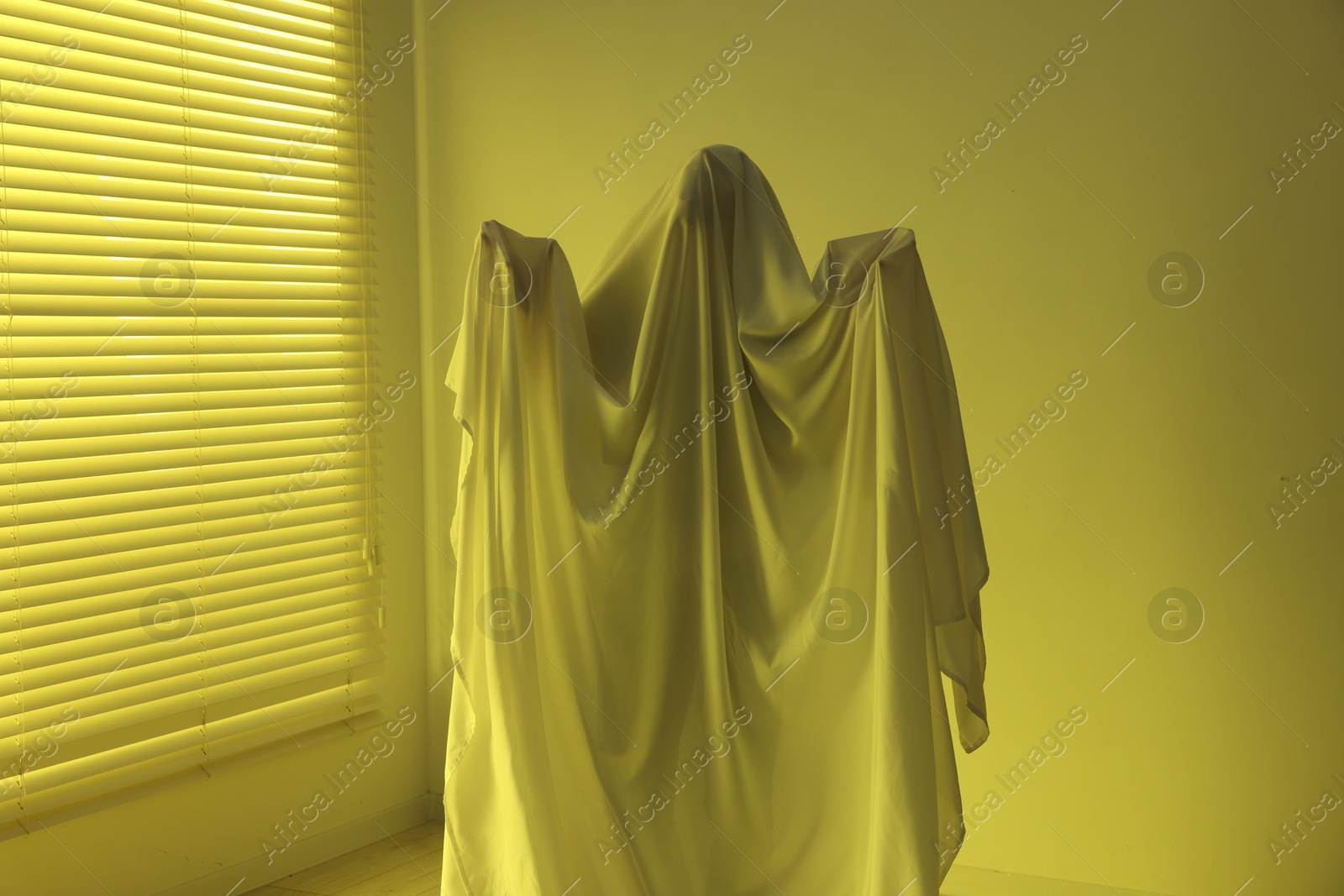 Creepy ghost. Man covered with white sheet indoors in yellow light Photo of Creepy ghost. Man covered with white sheet indoors in yellow light