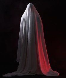 Photo of Creepy ghost. Man covered with white sheet on black background