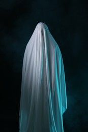 Photo of Creepy ghost. Man covered with white sheet in smoke on black background