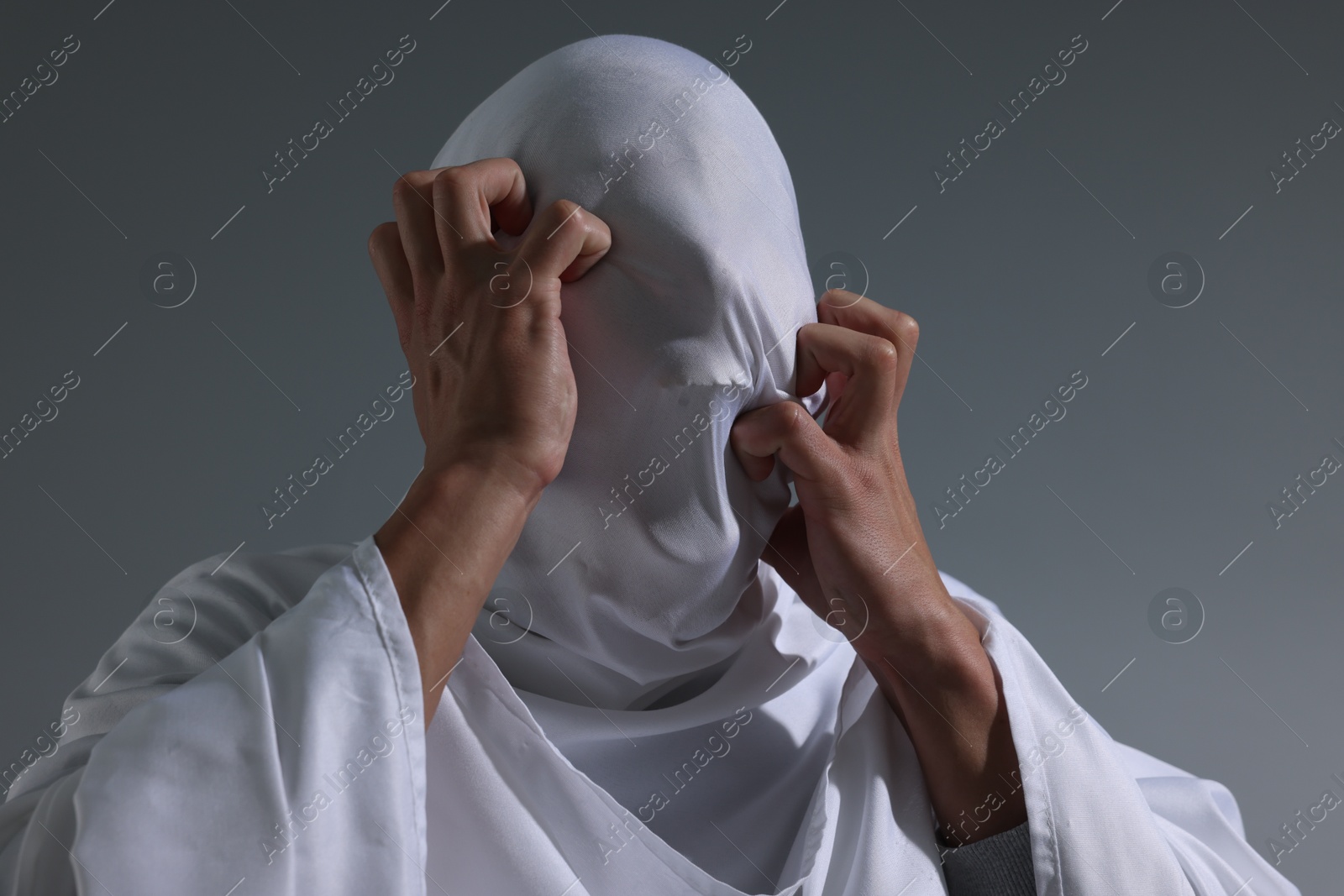Photo of Creepy ghost. Man covered with white sheet on light grey background