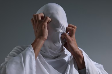 Photo of Creepy ghost. Man covered with white sheet on light grey background