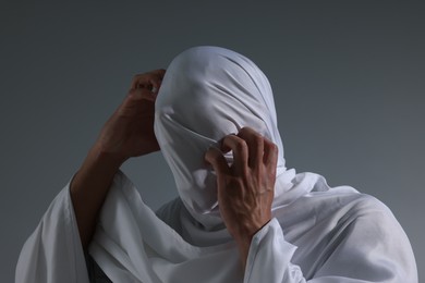 Photo of Creepy ghost. Man covered with white sheet on light grey background