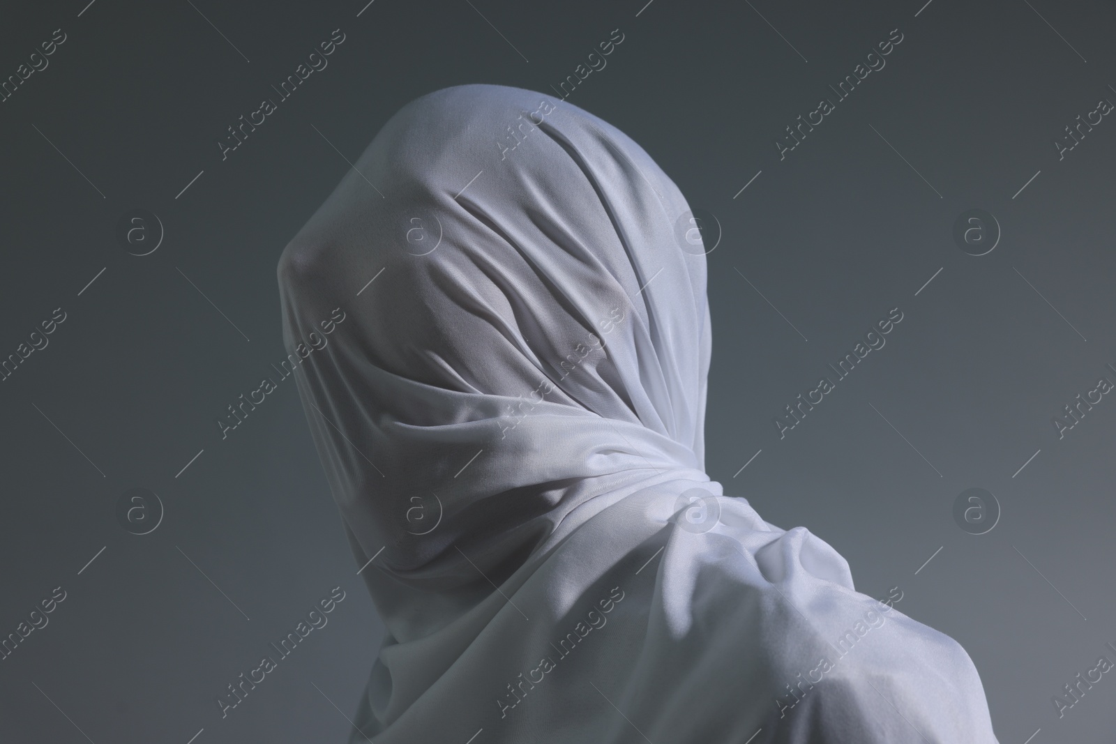 Photo of Creepy ghost. Man covered with white sheet on light grey background