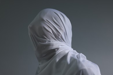 Photo of Creepy ghost. Man covered with white sheet on light grey background