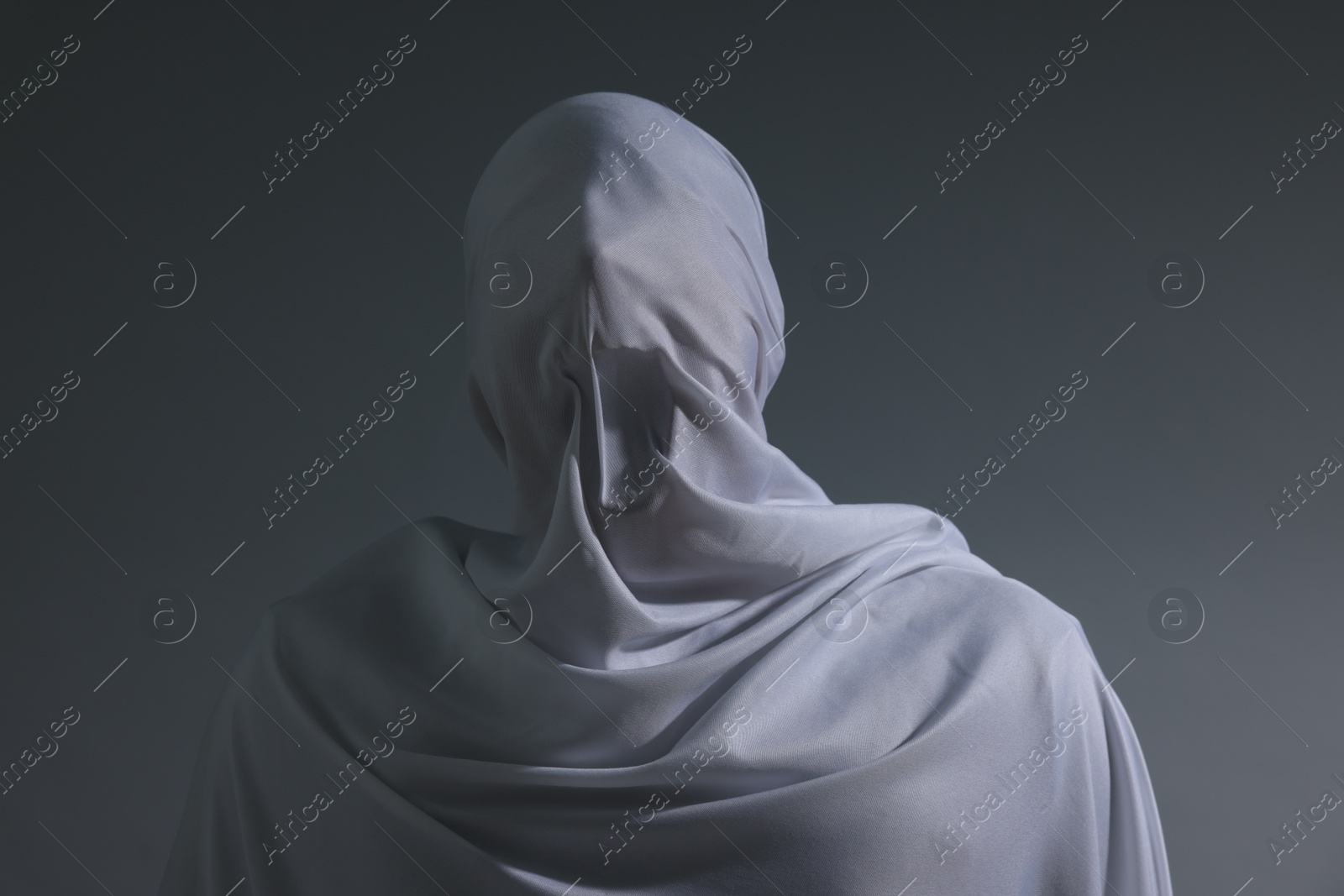 Photo of Creepy ghost. Man covered with white sheet on light grey background